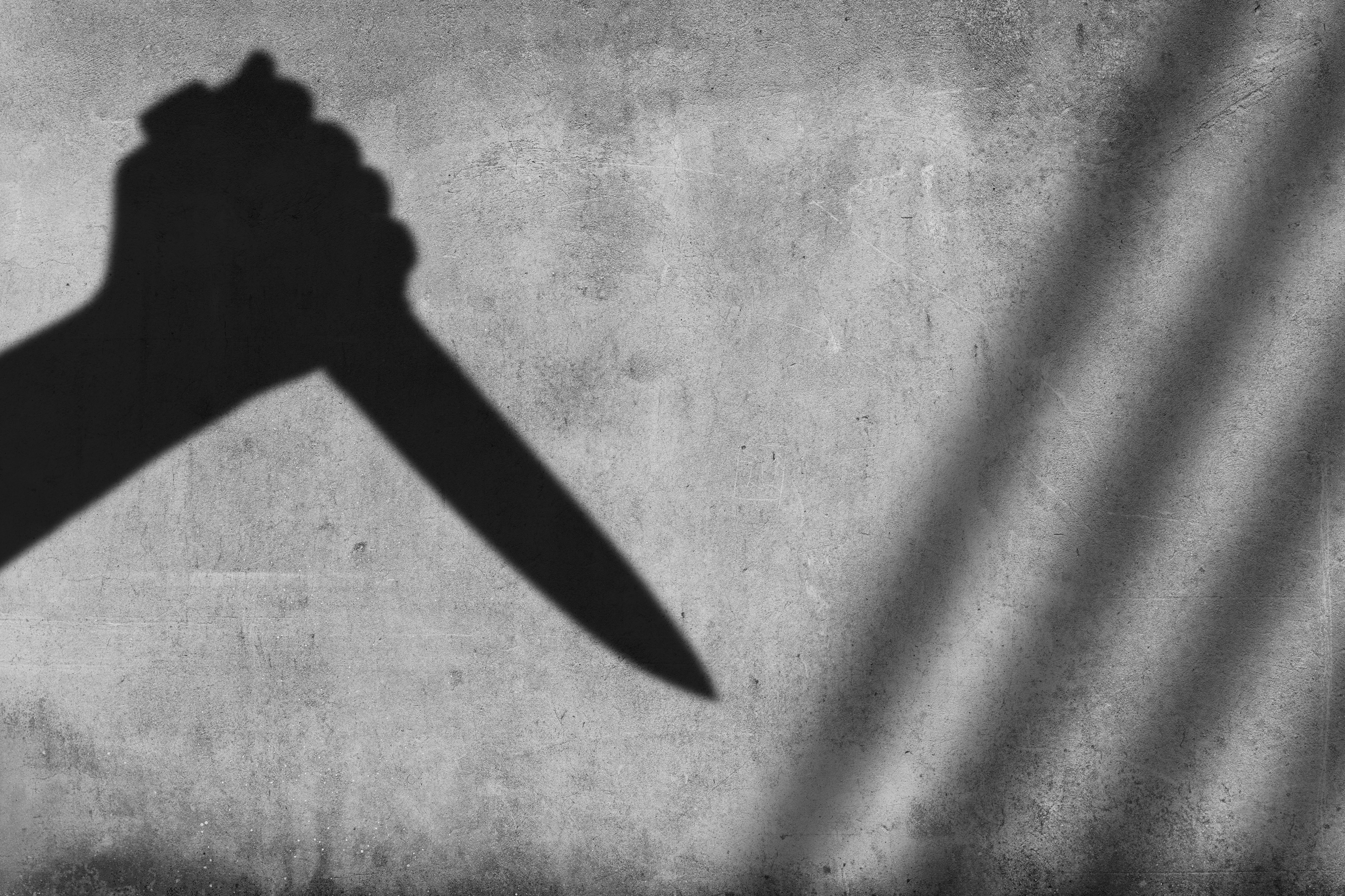 Shadow of the hand holding a knife on wall background - stock photo
