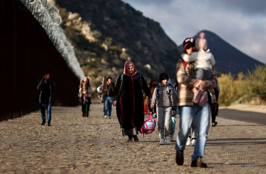 JACUMBA HOT SPRINGS, CALIFORNIA - DECEMBER 01: Asylum seeking migrants from Tajikistan (C) walk toward a makeshift camp to await processing by the U.S. Border Patrol after crossing into the United States past a gap in the border barrier December 1, 2023 in Jacumba Hot Springs, California. The remote community, with a population of 600, has seen a recent influx of hundreds of immigrants arriving daily and sheltering in makeshift camps in the desert cold as they await transfer to established U.S. Border Patrol detention centers which have limited capacity. (Photo by Mario Tama/Getty Images)