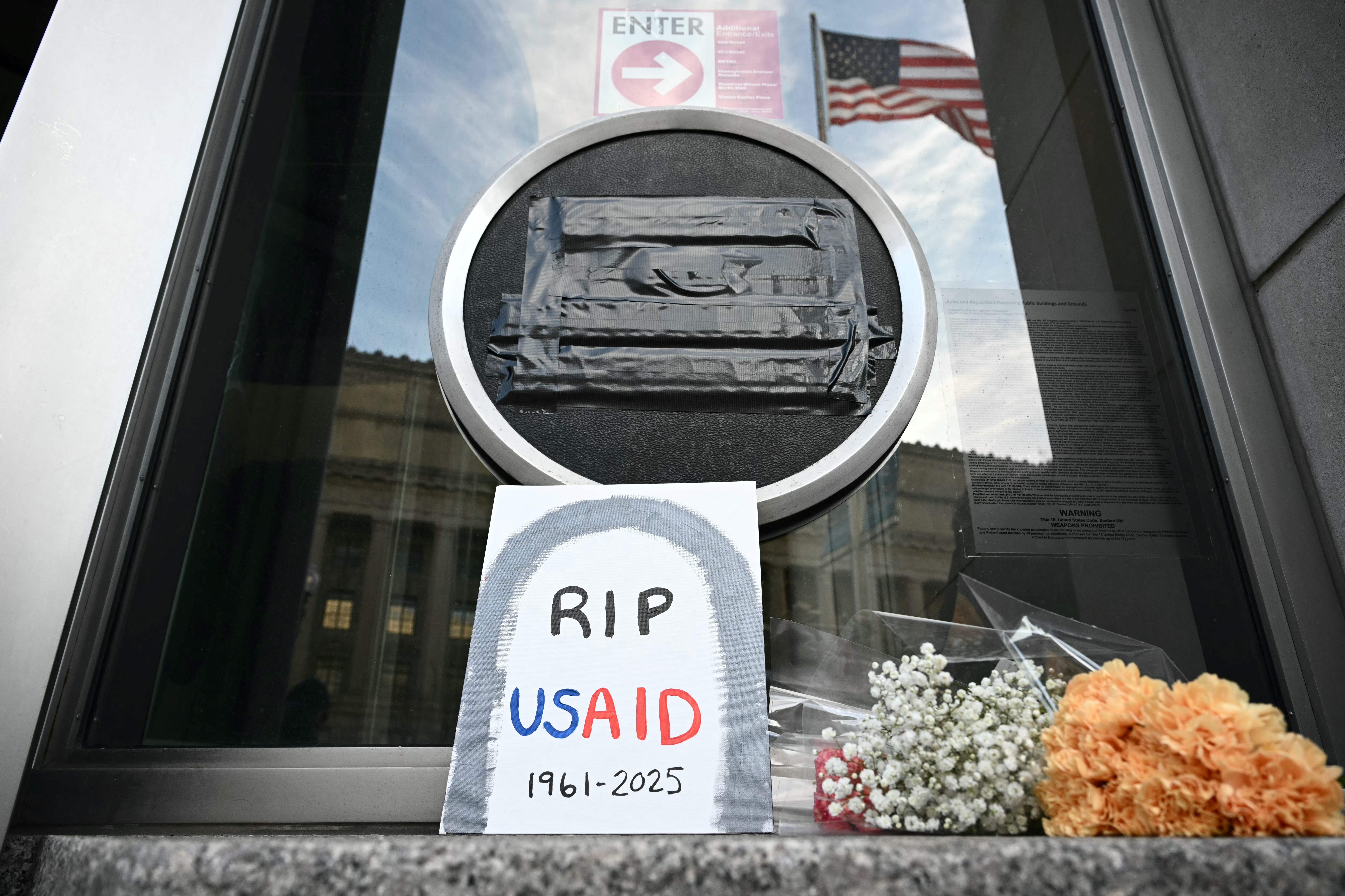 Tributes are placed beneath the covered seal of the US Agency for International Development (USAID) at their headquarters in Washington, DC, on February 7, 2025.